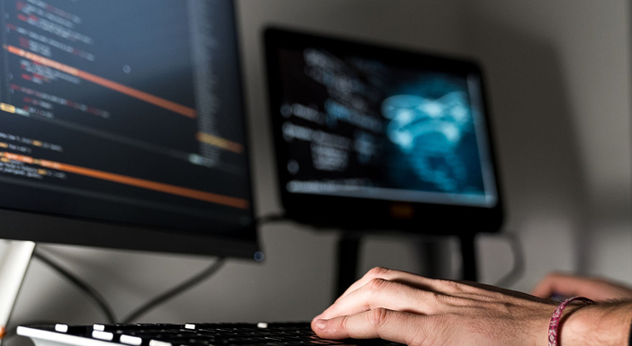 Person typing on keyboard with dual computer monitors displaying code.
