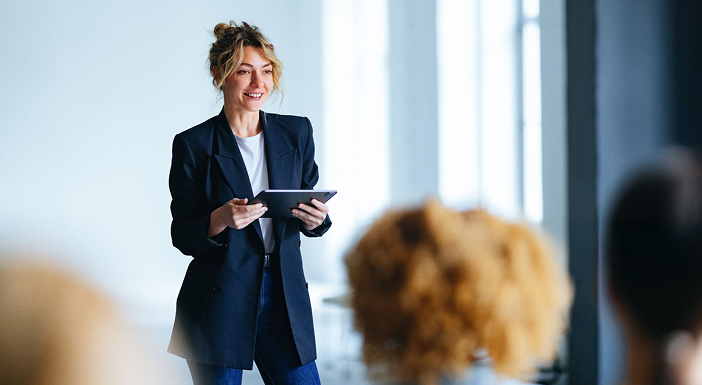 Person smiling, holding tablet, wearing black blazer in office setting.