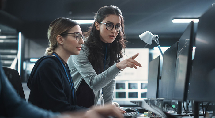 Two women collaborating at computer screens in modern office.
